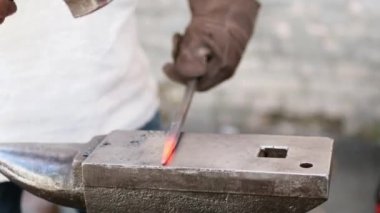 Özel giyinmiş bir nalbant, elinde çekiçle örse kızgın metal takıyor. Yakın plan.