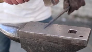 Özel giyinmiş bir nalbant, elinde çekiçle örse kızgın metal takıyor. Yakın plan.