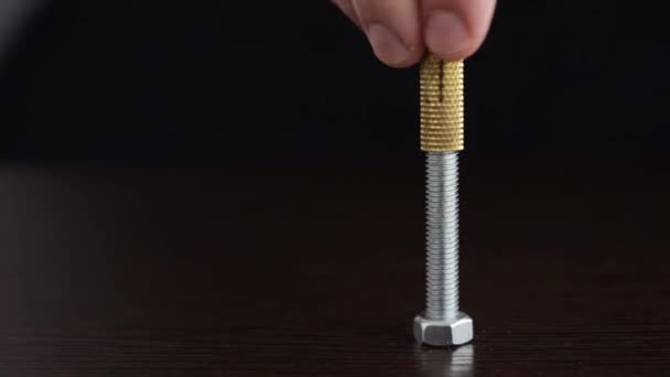 一个人的手指会转动一个金色的螺母 把它固定在一个有螺纹的螺栓上 并靠在一个深色的木制背景上 — 图库视频影像