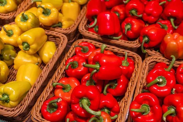 Vibrant red and yellow bell peppers in woven baskets on display at a market, showcasing fresh produce.