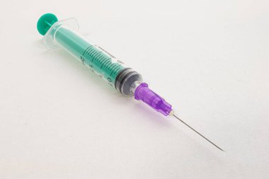 Mavi ve mor bileşenleri beyaz kağıdın üzerinde çapraz duran tıbbi bir şırınga..