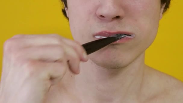 特写一个男人用黄色背景的黑色牙刷刷牙的特写 — 图库视频影像