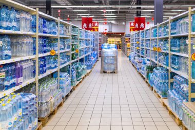 Kyiv, Ukraine - 03.07.2024: Shelves lined with various brands of bottled water in a Auchan supermarket with promotional signs, depicting consumer choice and plastic use. clipart
