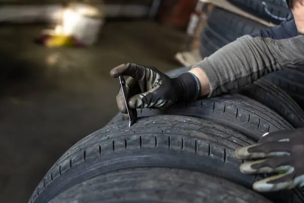 A mechanic\'s gloved hands using calipers to measure or assess the wear on a car tire in an automotive workshop.