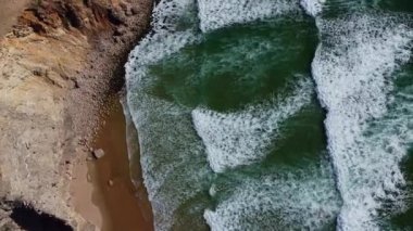 4K hava manzaralı okyanus dalgaları kayalık uçurumlar kumlu sahil, Portekiz Hava Aracı Videosu. 20 Nisan 2023 