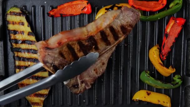 三骨肉牛排与烤蔬菜一起在烤架上翻滚 慢动作顶部视图 — 图库视频影像