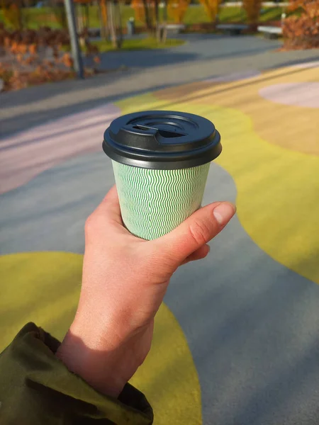 Paper cup with coffee in a woman hand. Time to drink coffee in city park. Coffee to go. Disposable paper cup with lid close-up. Delicious hot drink. photo was taken with smartphone camera