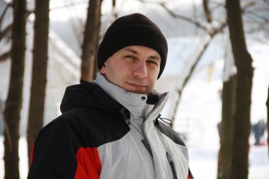 Karlı kış ormanlarında genç bir adamın portresi. Yakışıklı adam kameraya bakıyor ve gülümsüyor. Kış, Noel ve Yeni Yıl tatilleri, aktif yaşam tarzı, seyahat.