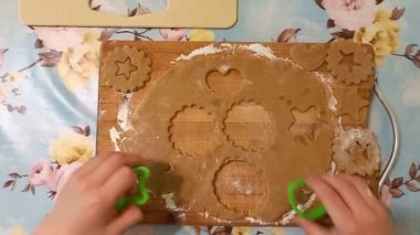 child participates in preparation of homemade gingerbread cookies. Closeup of a childs hand cutting out cookies using cookie cutters on cutting board. Delicious sweet homemade cake.