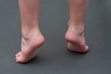 child is barefoot on mat. child does an exercise for feet, standing on tiptoes. Back view. Prevention of flat feet in children. Health care.