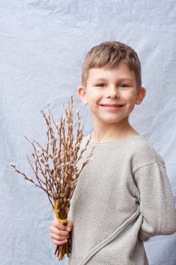 Portrait of handsome preschool boy with bouquet of spring flowers on blue background. child holding branches of flowering willow in hand, smiling. Happy easter. Palm Sunday. Springtime.