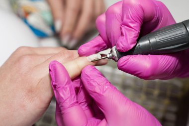 Güzellik salonunda manikür yapma süreci. Manikürcü elektrikli çivi matkabı ve tırnak tedavisi kullanıyor. Profesyonel manikür, güzellik elleri. Sahip ve istemcinin ellerinin kapatılması.