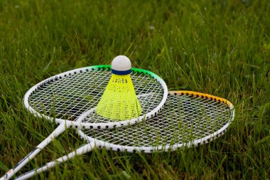 Badminton yeşil çimlerin üzerine sarı mekikli horoz ve raket koymuştu. Spor konsepti. Açık havada aktif badminton oyunu. Spor malzemeleri..