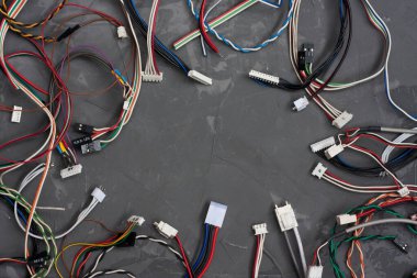 Gri beton arka planda bağlantıları olan renkli kablolar ve kablolar. Renkli farklı bilgisayar ve diğer kablolar. Telekomünikasyon. Kartpostal için boşluk, mesaj için boşluk. Düz çizgi