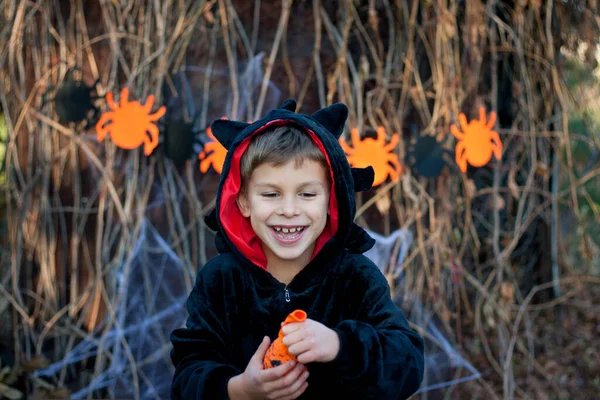Happy Halloween. Portrait of happy preschool boy in black dragon carnival costume. child having fun, inflating balloon. Halloween party outdoor, autumn