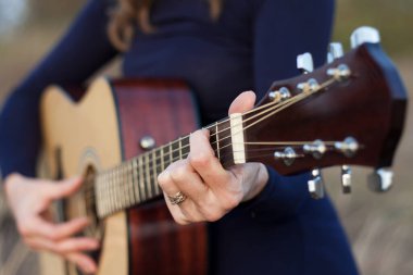 Akustik gitar çalan bir kadının ellerinin yakın çekimi. Açık hava eğlencesi, yaratıcı bir akşam, ılık bir sonbahar, gün batımı. Romantik bir ruh hali. Seçici Odaklanma