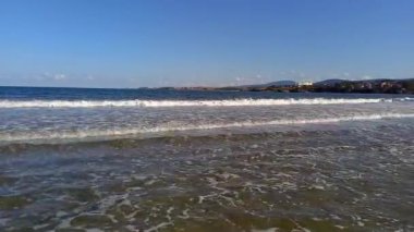 Güneşli yaz gününde resimli deniz manzarası. Küçük dalgalar kıyıya vuruyor, dağlar ve tatil köyü ufukta görünüyor. Bulgaristan, Kiten kasabası, Güney Sahili Karadeniz kıyısında tatiller