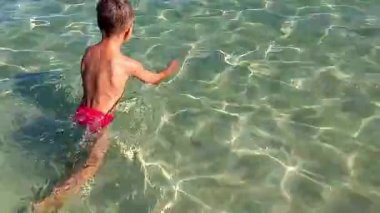 Güneşli bir yaz gününde sığ sularda yüzen beyaz çocuk. Mutlu çocuk yüzüyor. Sağlıklı bir yaşam tarzı. Denizde yaz tatili