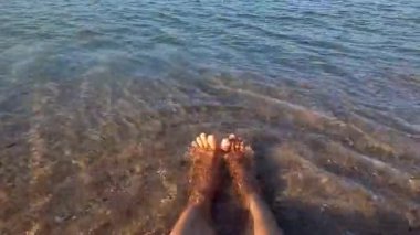 Güneşli bir günde kumsalda dinlenen iki kadın bacağı görüntüsü. Kumsalda ayakları deniz suyunda oturan bir kadın. Seyahat konsepti. Denizde tatiller.