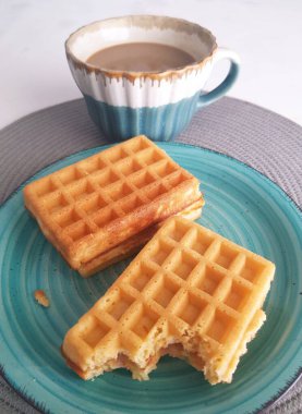 Bir fincan çay tabağında waffle ve bir fincan süt.