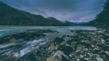Dağ ormanı yakınlarındaki bir nehirde akan suyun 4K UHD zaman çizelgesi. Büyük kayalar ve hızlı bulutlar hareket ediyor..