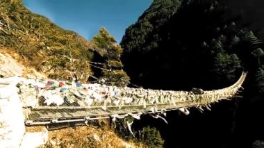 Khumbu vadisindeki en büyük asma köprü renkli Tibet dua bayraklarıyla. Vahşi Himalayalar yüksek irtifa doğa ve dağ vadisi. Ağaçlarla kaplı kayalık yamaçlar. Trek alanı ana kampa gidiyor.