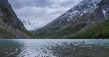 4K UHD dağ gölü zaman ayarlı yaz veya sonbahar saatlerinde. Vahşi doğa ve kırsal dağ vadisi. Çam ağaçlarından oluşan yeşil orman ve gökyüzünde hızlı bulutlar. Motorlu doli kaydırma hareketi