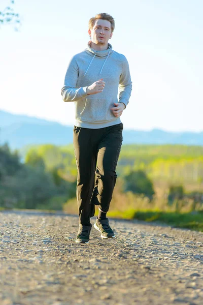 Running man jogging in rural nature at beautiful summer day. Sport fitness model caucasian ethnicity training outdoor.