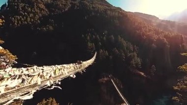 Khumbu vadisindeki en büyük asma köprü renkli Tibet dua bayraklarıyla. Vahşi Himalayalar yüksek irtifa doğa ve dağ vadisi. Ağaçlarla kaplı kayalık yamaçlar. Trek alanı ana kampa gidiyor.