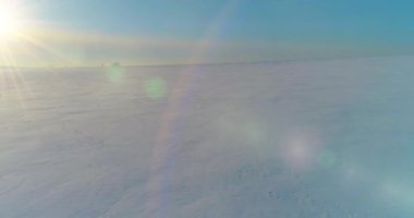 Soğuk kış kutup bölgesinin insansız hava görüntüsü, ufukta karla kaplı ağaçlar, buz nehri ve güneş ışınları. Aşırı düşük sıcaklık havası.