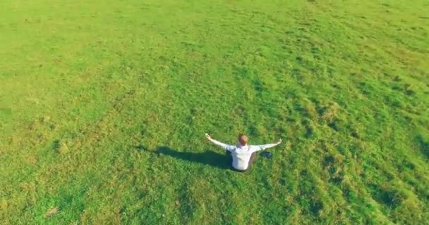 空中的观点 在黄色的乡间田野 低轨道绕着人类坐在绿草上 带着记事本 随意穿和禅定双手向上 太阳光 拨号运动 — 图库视频影像