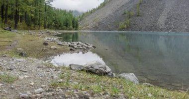 4K UHD dağ gölü zaman ayarlı yaz veya sonbahar saatlerinde. Vahşi doğa ve kırsal dağ vadisi. Çam ağaçlarından oluşan yeşil orman ve gökyüzünde hızlı bulutlar. Motorlu doli kaydırma hareketi
