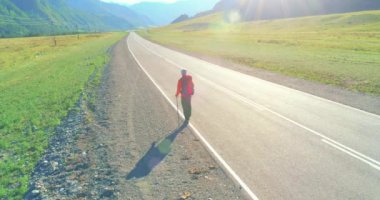 Hava 4K UHD görüntüsü. Asfalt yolda yürüyen otostopçu turist üzerinde alçak irtifa uçuşu. Büyük bir kırsal vadi ve yaz günü güneşli bir çayır. Sırt çantalı gezgin..