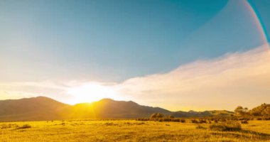 Yaz ya da sonbahar günbatımında dağdaki çayır zaman atlaması. Vahşi doğa ve kırsal alan. Bulutların hareketi, yeşil çimenler ve güneş ışınları. Motorlu Panorama