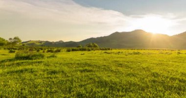 Yaz ya da sonbahar günbatımında dağdaki çayır zaman atlaması. Vahşi doğa ve kırsal alan. Bulutların hareketi, yeşil çimenler ve güneş ışınları. Motorlu Panorama