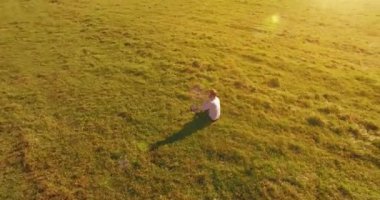 Havadan bakış açısı. Yeşil çimlerin üzerinde oturan, sarı kırsal alanda not defteri olan ve telefonla konuşan bir adam. Günlük kıyafet. Güneş ışınları. Radikal hareket.