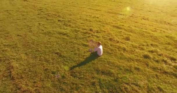 空中展望台 黄色の田園地帯にノートパッドと緑の芝生の上に座って電話で話す人の周りの低軌道飛行 普段着 太陽光線 放射線運動 — ストック動画
