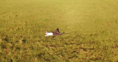 Havadan bakış açısı. Sarı kırsal alanda yeşil çimlerin üzerinde dizüstü bilgisayarı olan bir adam etrafında alçak yörüngeden uçuyordu. Sıradan giyinmiş. Güneş ışınları. Radikal hareket.