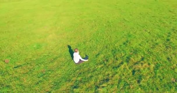 空中的观点 在黄色的乡间田野 低轨道绕着人类坐在绿草上 带着记事本 随意的穿着和禅定的姿势 太阳光 拨号运动 — 图库视频影像