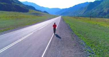 UHD 4K hava görüntüsü. Mükemmel asfalt yolda sporcunun önünde alçak irtifa uçuşu. Dağda gün doğumu. Yeşil çayır ve ufukta güneş ışığı. Hızlı yatay hareket.