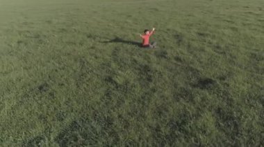 UHD 4K hava görüntüsü. Yeşil çimlerde spor yogacısı üzerinde alçak irtifa radyal uçuş. Dağda gün batımı. Yeşil çayır ve ufukta güneş ışığı. Hızlı yörünge hareketi. Düz renk. Renk notu yok