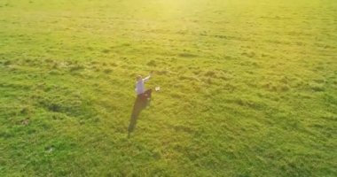 Havadan bakış açısı. Yeşil çimlerde oturan ve kırsal alanda not defteri olan bir adamın etrafında alçak yörünge uçuşları. Gündelik kıyafet ve Zen meditasyonu. Eller havada. Güneş ışınları. Radikal hareket.