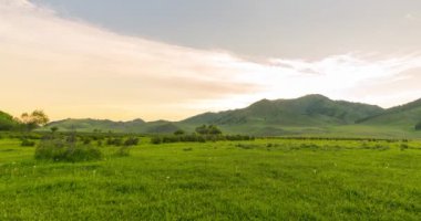 Yaz ya da sonbahar gündoğumunda dağdaki çayır zaman atlaması. Vahşi doğa ve kırsal alan. Bulutların hareketi, yeşil çimenler ve güneş ışınları. Motorlu Panorama