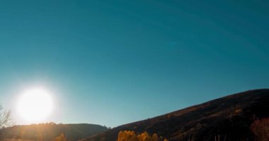 4k dağ çayırı yaz ya da sonbahar günbatımında zaman aşımına uğrar. Vahşi doğa ve kırsal alan. Açık gökyüzü, ağaçlar, yeşil ve sarı çimenler, ufukta güneş ışığı. Motorlu kaydırma hareketi.