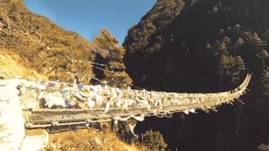 Khumbu vadisindeki en büyük asma köprü renkli Tibet dua bayraklarıyla. Vahşi Himalayalar yüksek irtifa doğa ve dağ vadisi. Ağaçlarla kaplı kayalık yamaçlar. Trek alanı ana kampa gidiyor.