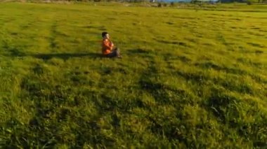 UHD 4K hava görüntüsü. Yeşil çimlerde spor yogacısı üzerinde alçak irtifa radyal uçuş. Dağda gün batımı. Yeşil çayır ve ufukta güneş ışığı. Hızlı yörünge hareketi.