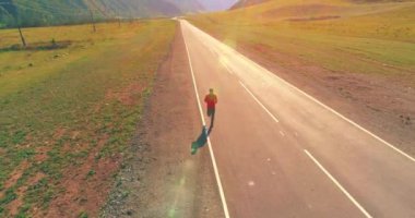 UHD 4K hava görüntüsü. Mükemmel asfalt yolda sporcunun önünde alçak irtifa uçuşu. Dağda gün doğumu. Yeşil çayır ve ufukta güneş ışığı. Hızlı yatay hareket.
