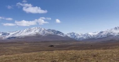 Güneş hareketinin 4K UHD zaman dilimi kristal berrak gökyüzünde ve karlı dağın tepesinde bulutlar. Sonbahar yüksek rakımlı çayırlarda sarı çimenler. Uçsuz bucaksız. Kamera hareketi