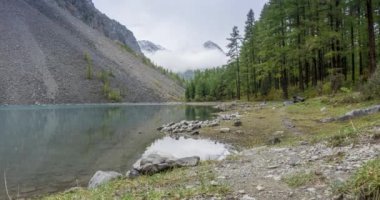 4K UHD dağ gölü zaman ayarlı yaz veya sonbahar saatlerinde. Vahşi doğa ve kırsal dağ vadisi. Çam ağaçlarından oluşan yeşil orman ve gökyüzünde hızlı bulutlar. Motorlu doli kaydırma hareketi