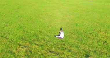 Havadan bakış açısı. Yeşil çimlerin üzerinde oturan, sarı kırsal alanda not defteri olan ve telefonla konuşan bir adam. Günlük kıyafet. Güneş ışınları. Radikal hareket.